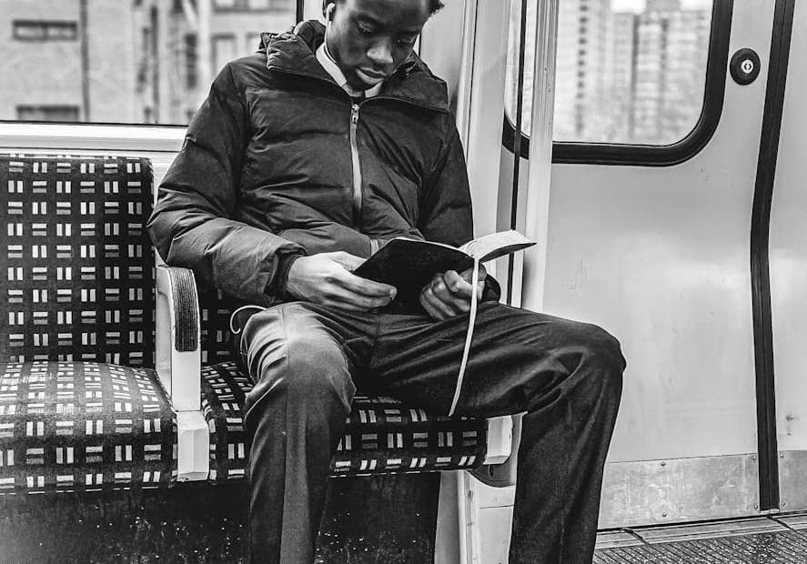 young man in suit reads book in tram